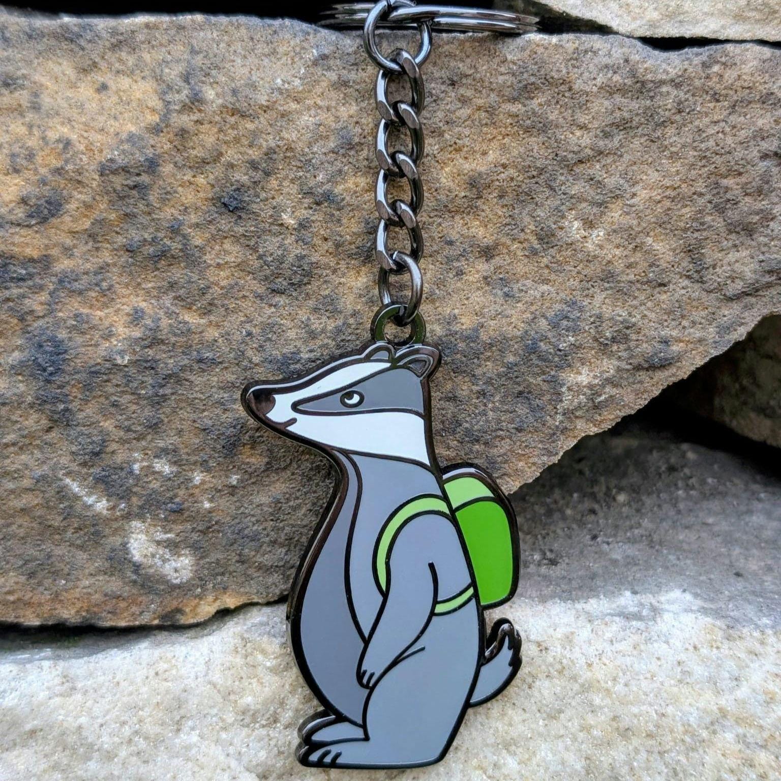 Keychain with a badger design wearing a green backpack against a stone background