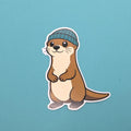 Sticker of cartoon otter wearing a blue hat on a teal background