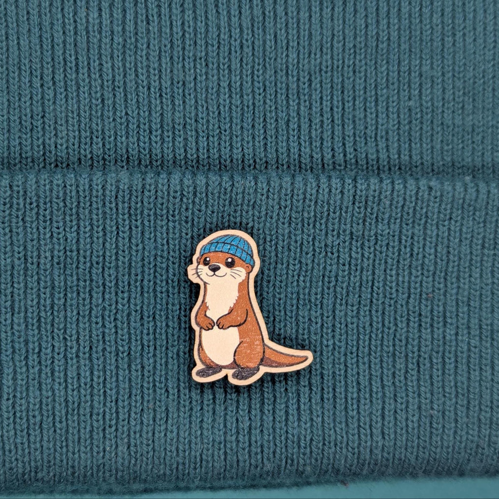 otter wooden pin badge on a beanie hat in the background