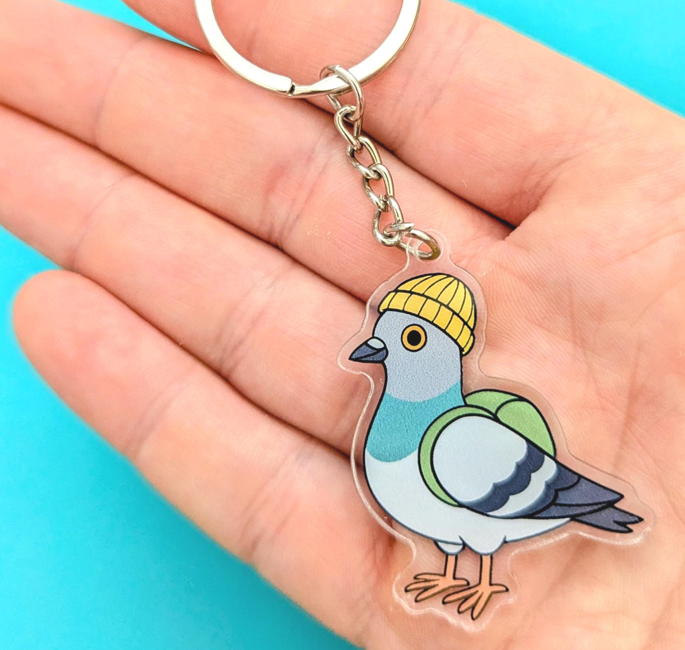 Acrylic pigeon keyring wearing a yellow hat held in a hand against a blue background
