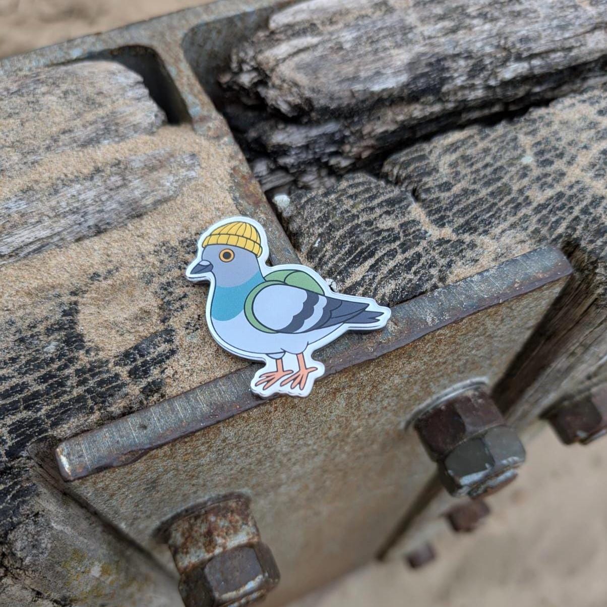 Fridge magnet of a pigeon wearing a yellow beanie on a rusty metal surface