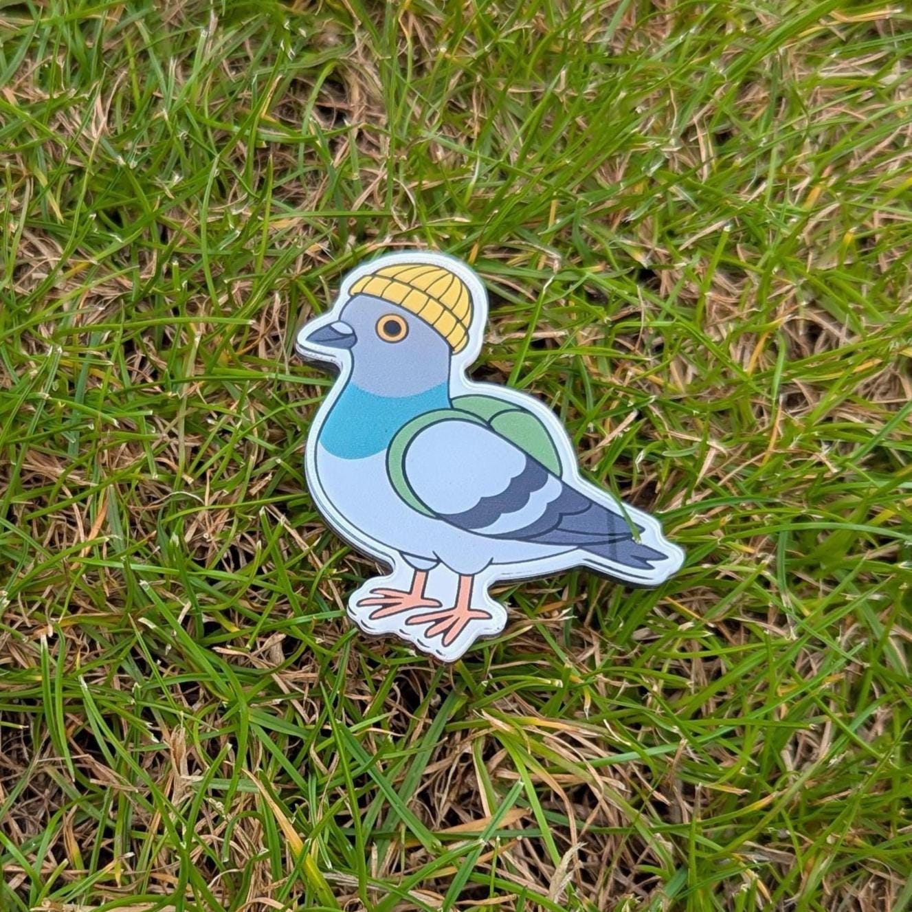 Fridge magnet of urban pigeon wearing a yellow beanie on grass