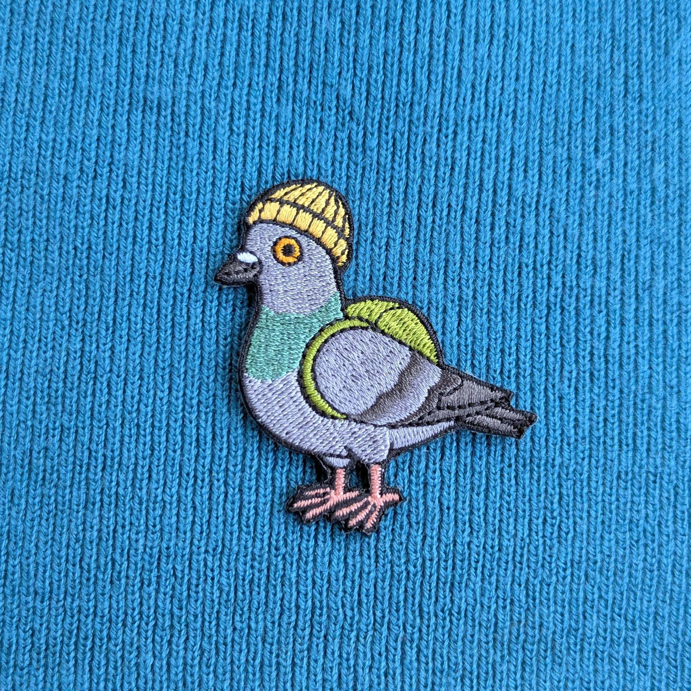 Embroidered pigeon wearing a yellow beanie on blue fabric