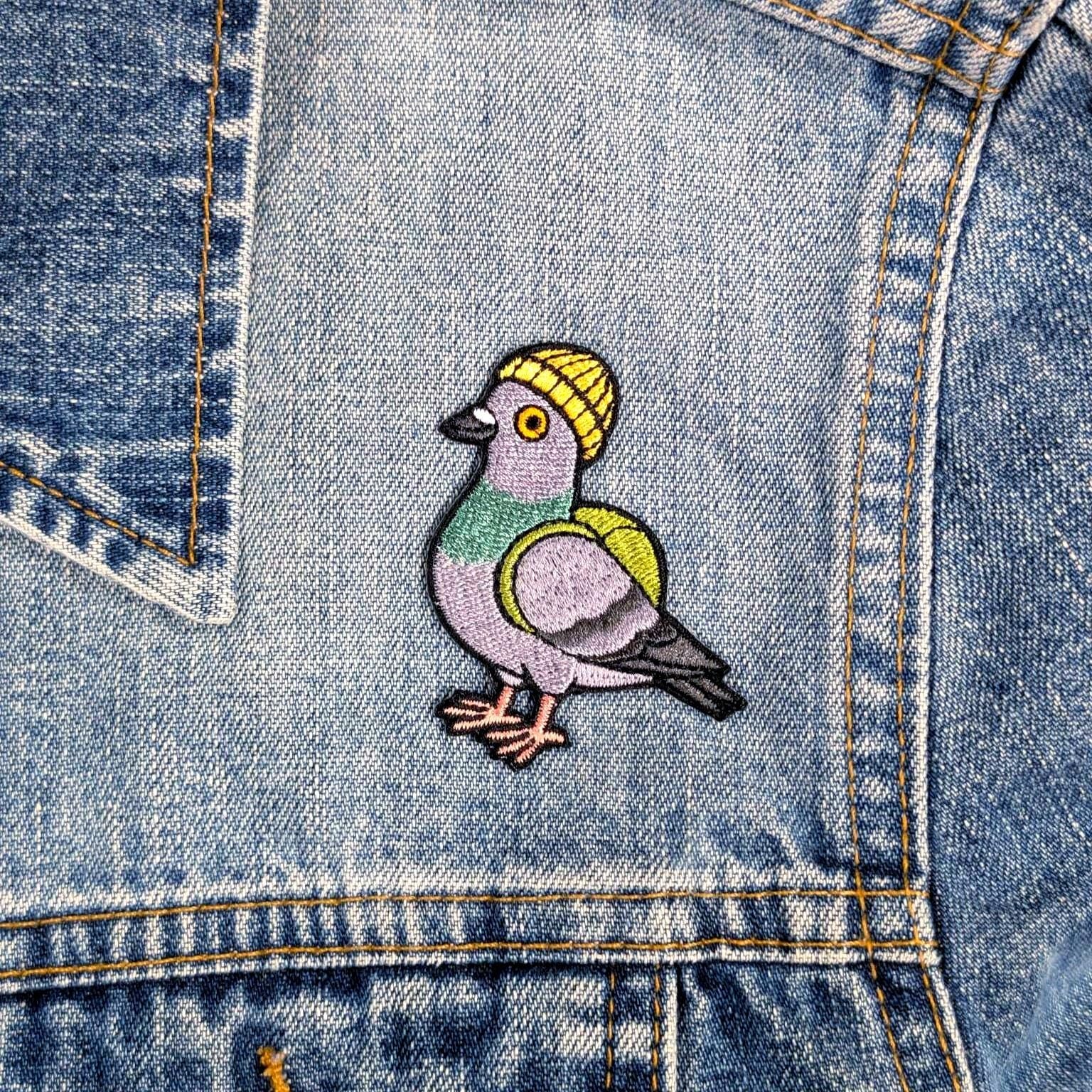 Embroidered pigeon wearing a yellow beanie on a denim jacket.