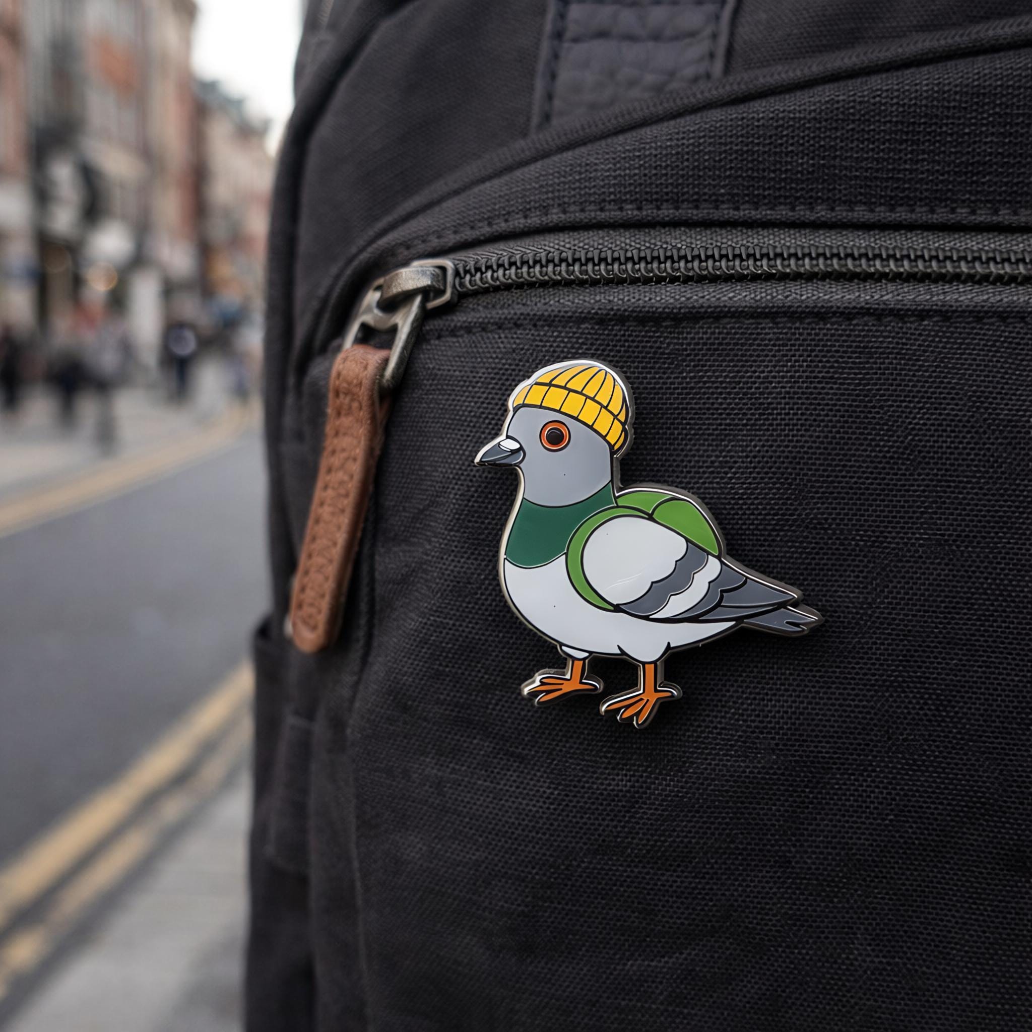 Pigeon pin with a yellow hat on a black backpack with a blurred street background