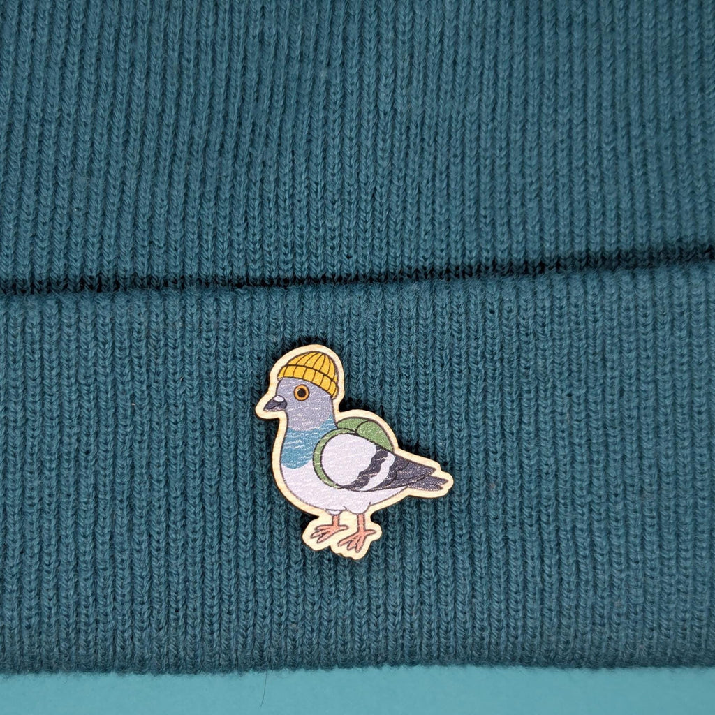Wooden pin of a pigeon wearing a yellow hat on a teal knitted fabric background