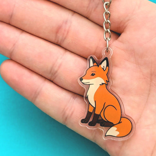 Fox keychain held in a hand with a blue background