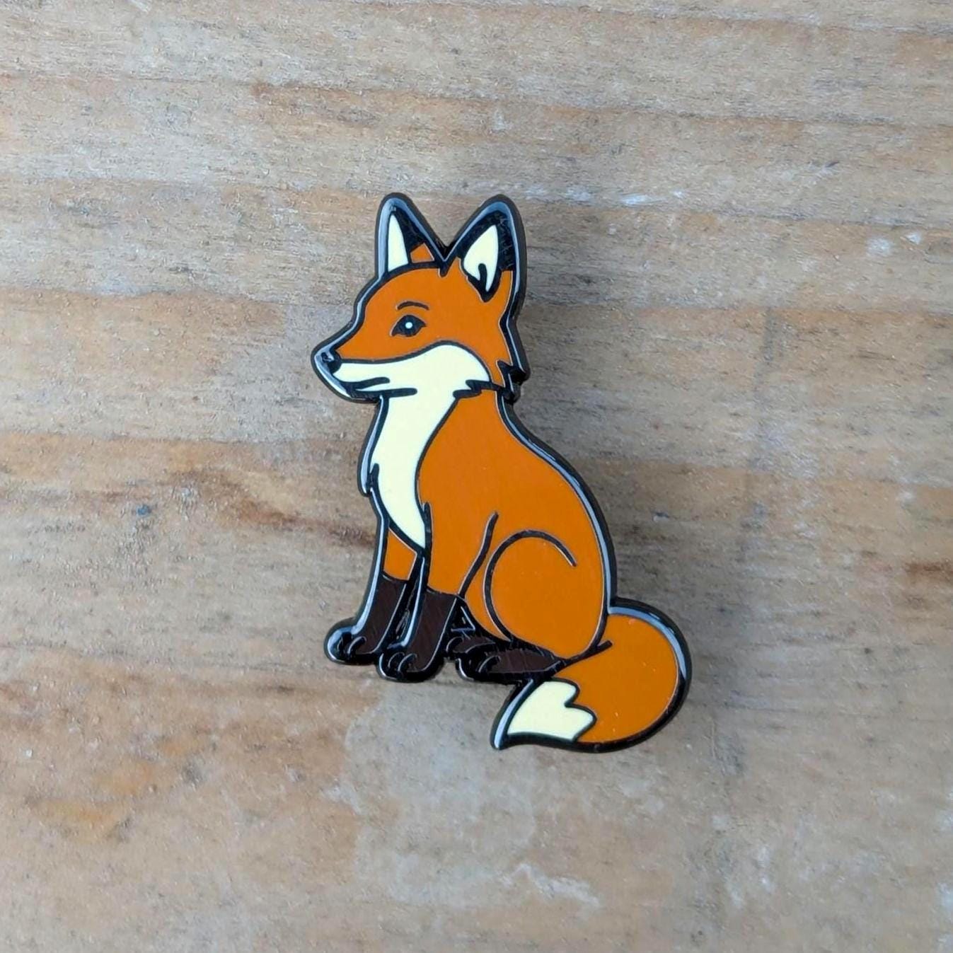 Fox-shaped enamel pin on a wooden surface
