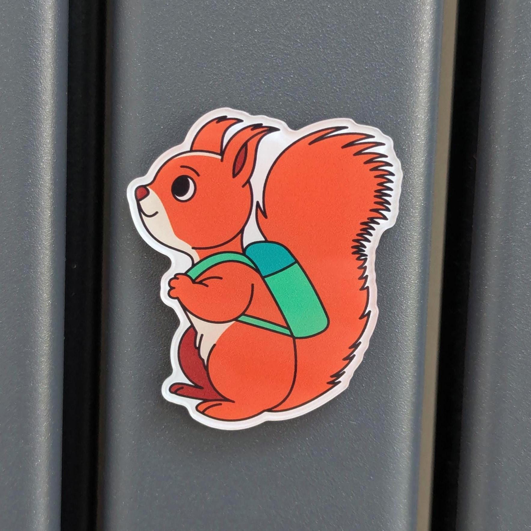 Fridge magnet of a red squirrel with a green backpack on a metallic surface