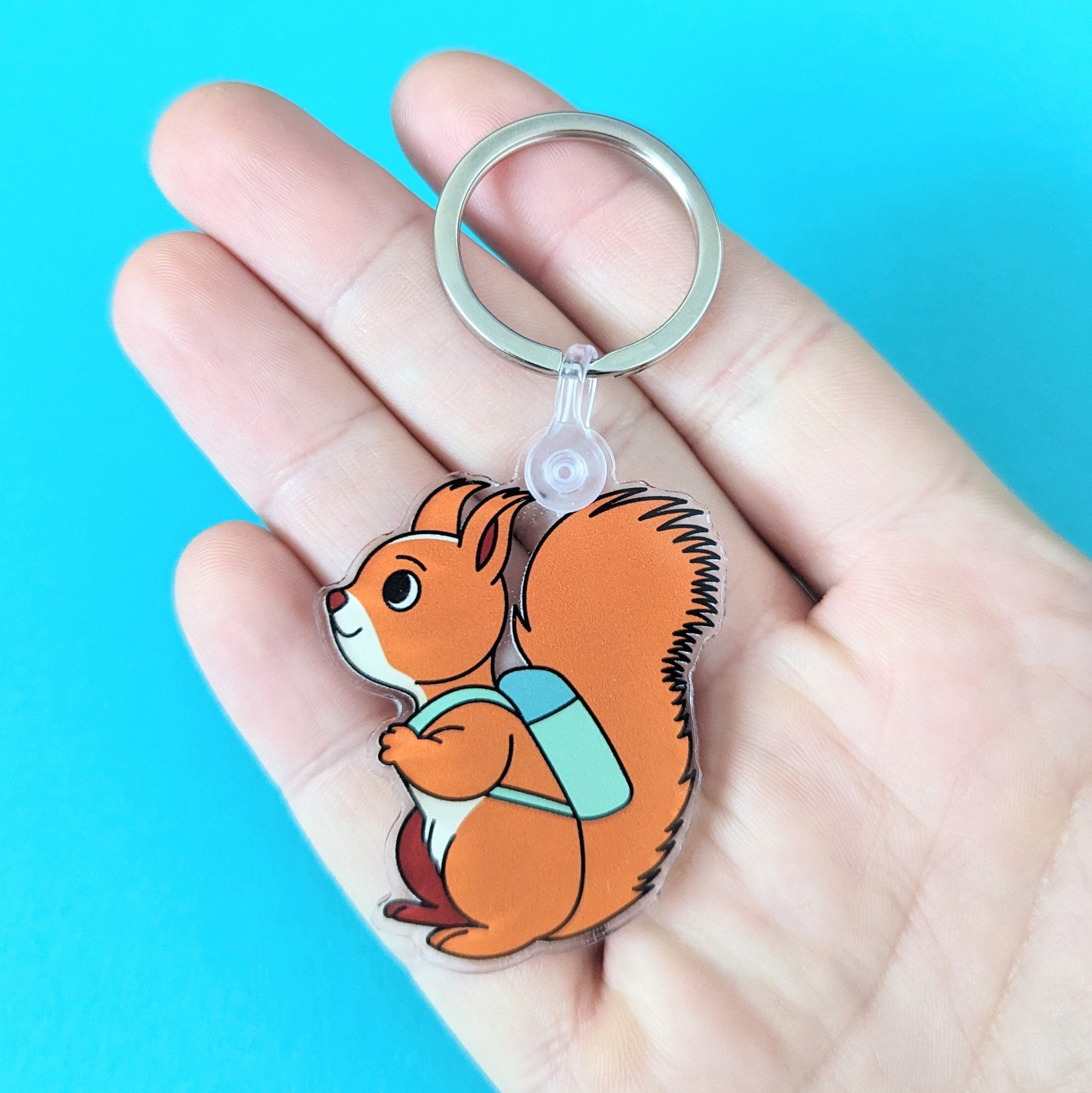 Squirrel keychain held in a hand against a blue background