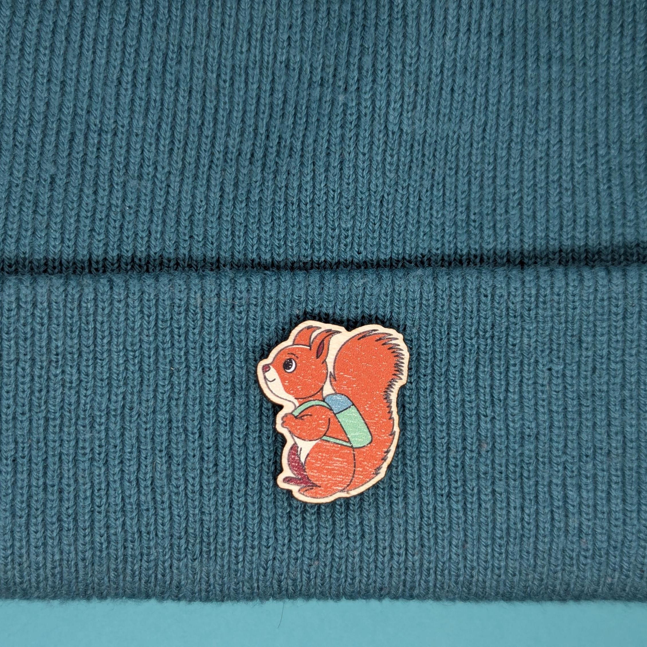 Red squirrel wooden pin on a textured teal fabric background