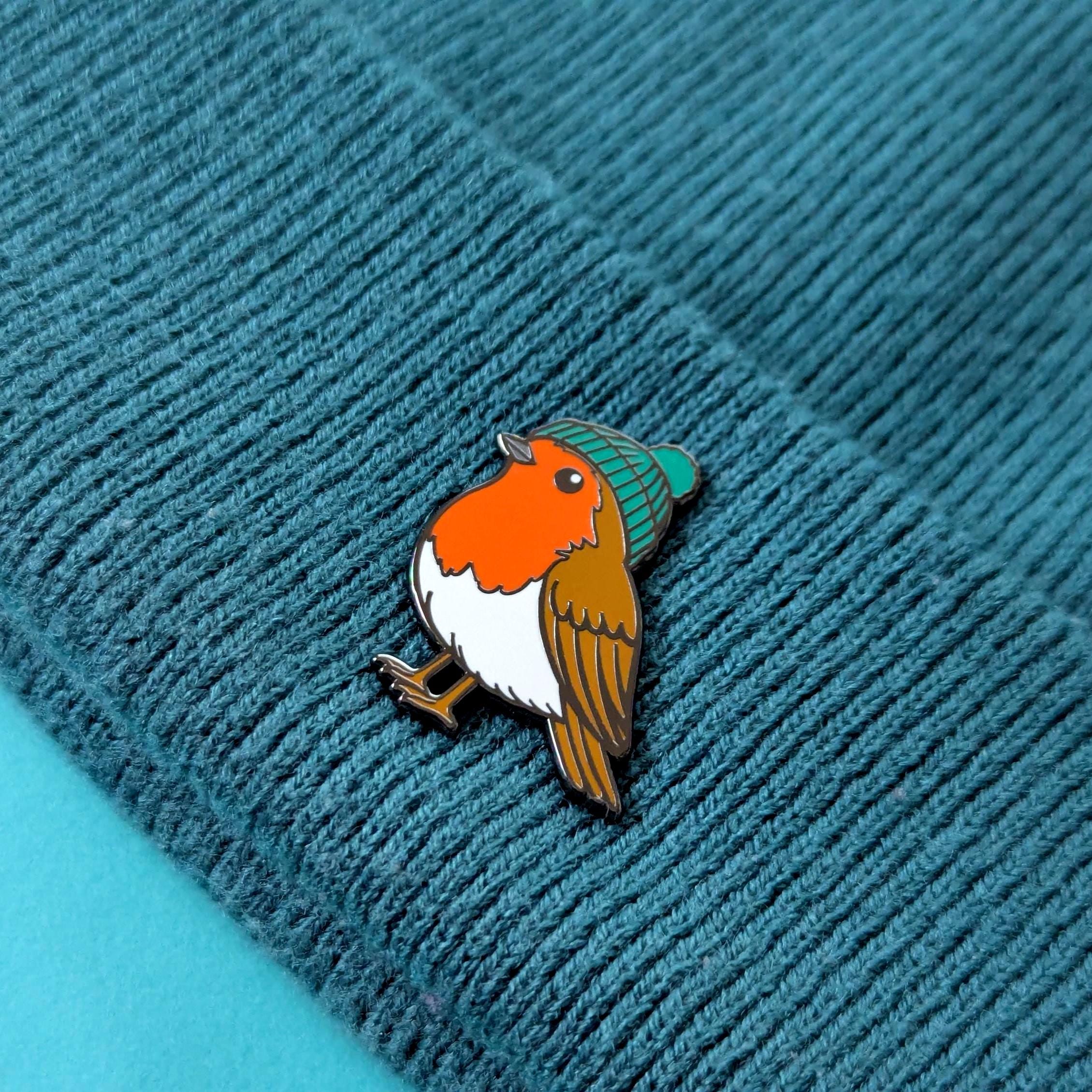 Robin bird pin with a green hat on a textured blue surface