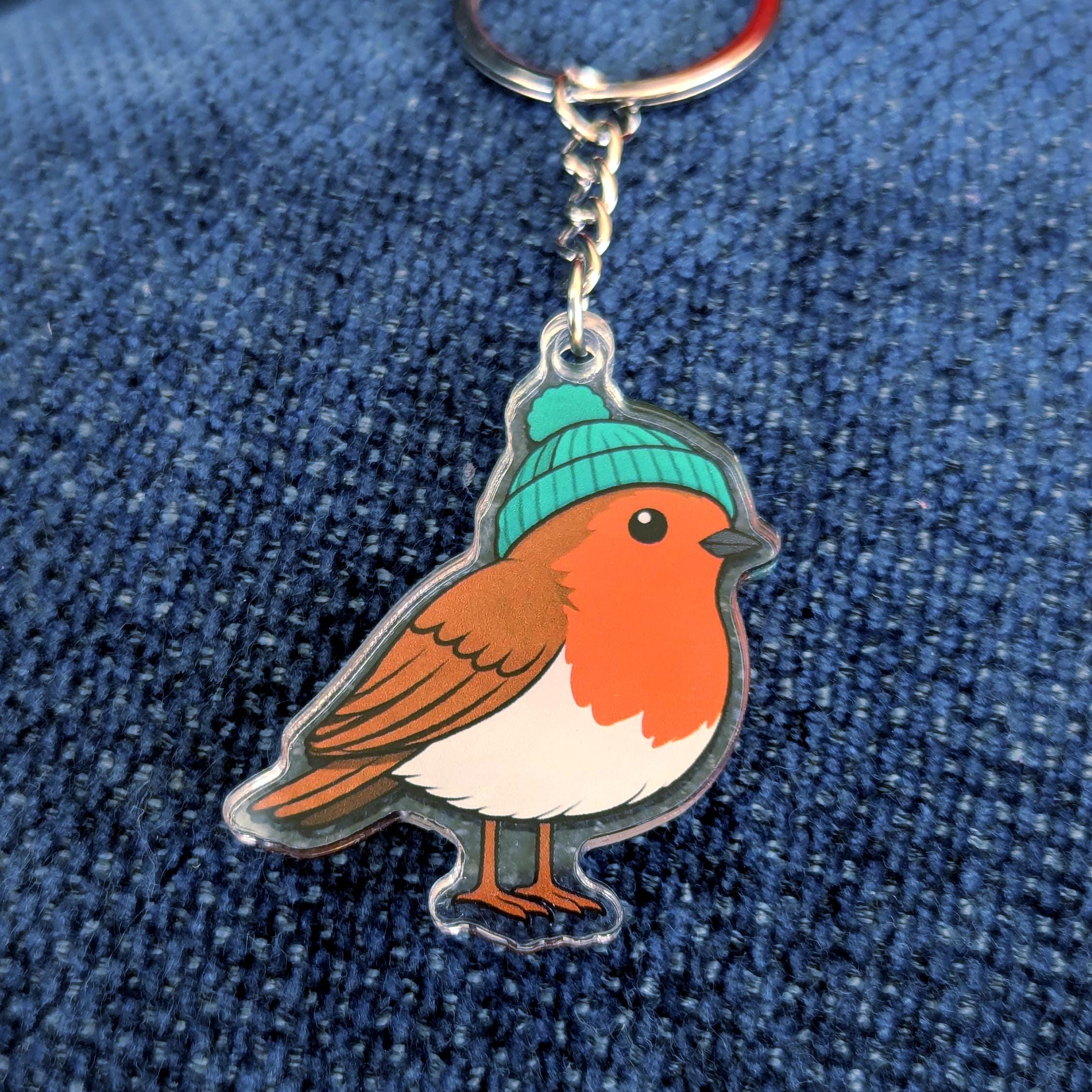 Keychain with a robin design wearing a green beanie on a blue denim background