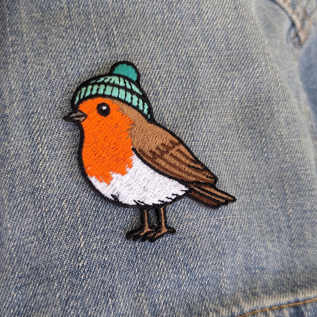 Embroidered patch of a robin wearing a knitted hat on denim fabric.
