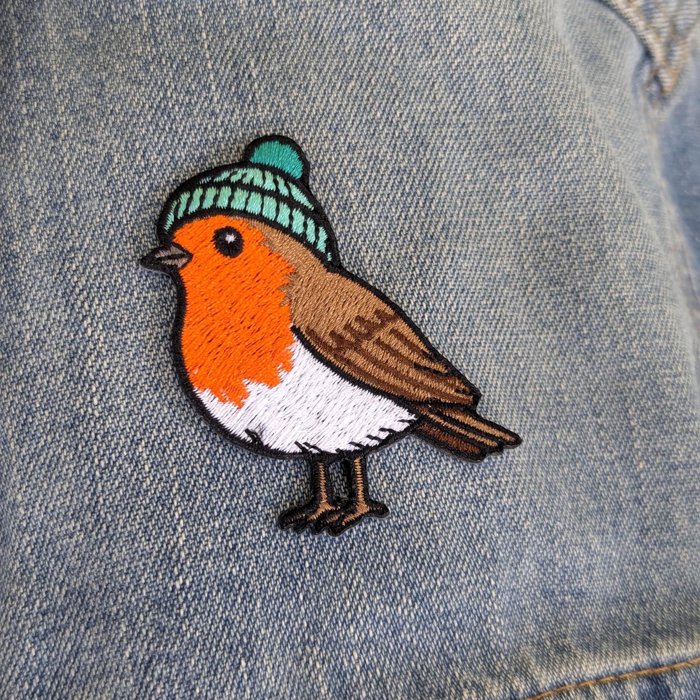 Embroidered patch of a robin wearing a knitted hat on denim fabric.