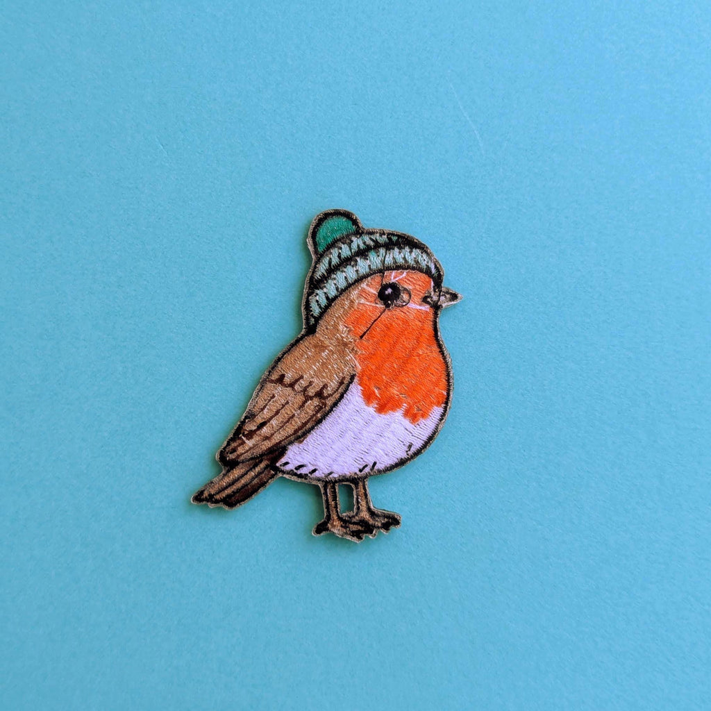 Back of embroidered patch of a robin wearing a knitted hat on a blue background