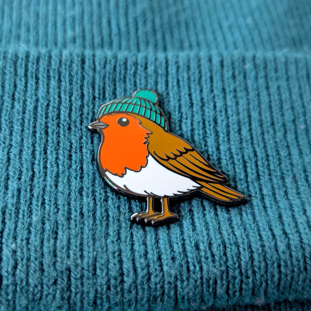 Robin enamel pin with a green beanie on a teal textured background