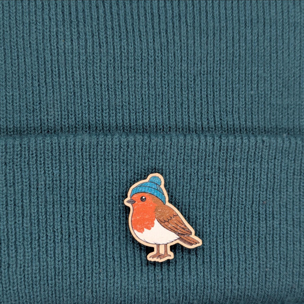 Robin bird pin with a blue beanie on a teal knitted fabric background