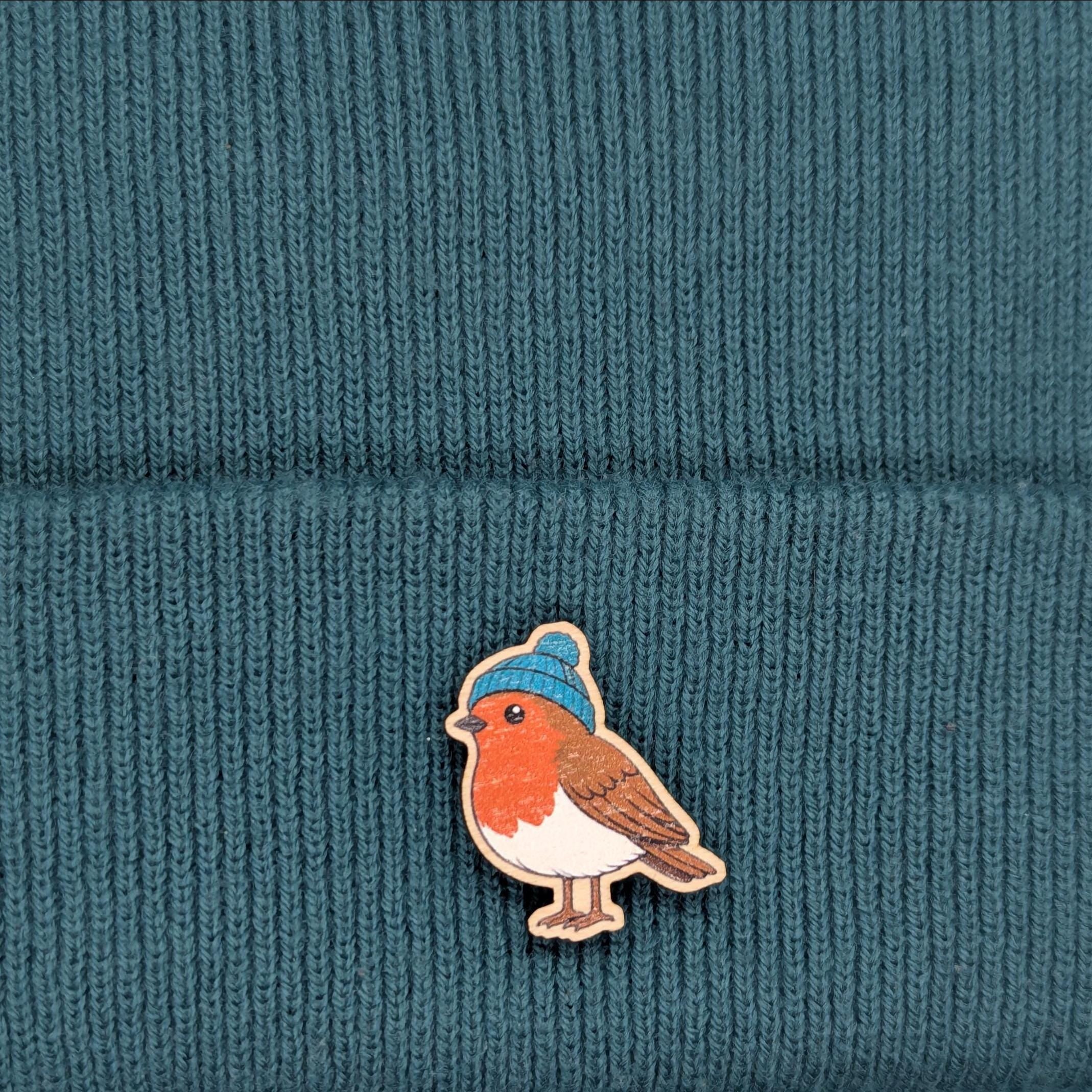 Robin bird pin with a blue beanie on a teal knitted fabric background