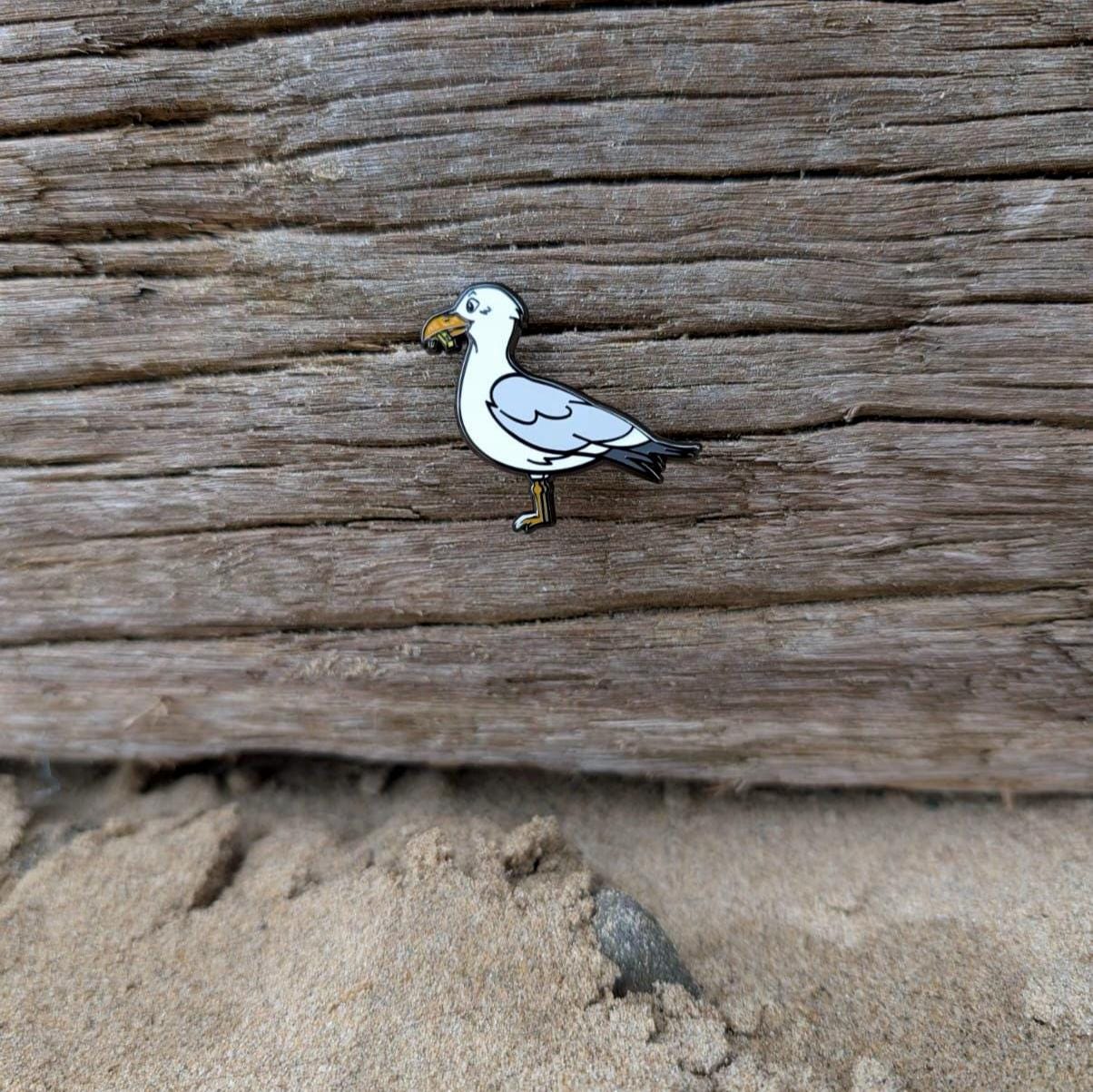 Seagull pin on a wooden surface with sand in the background