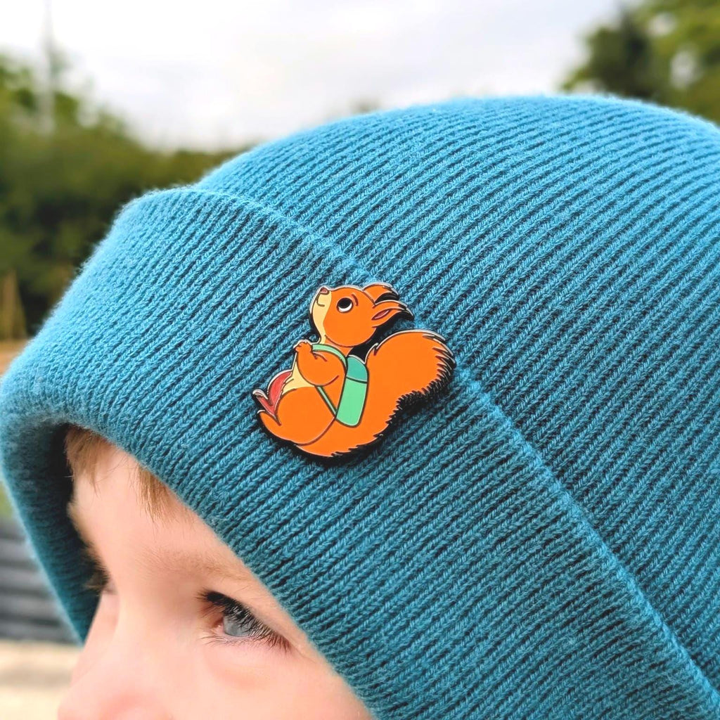 Blue beanie with a cartoon squirrel pin worn by a child outdoors