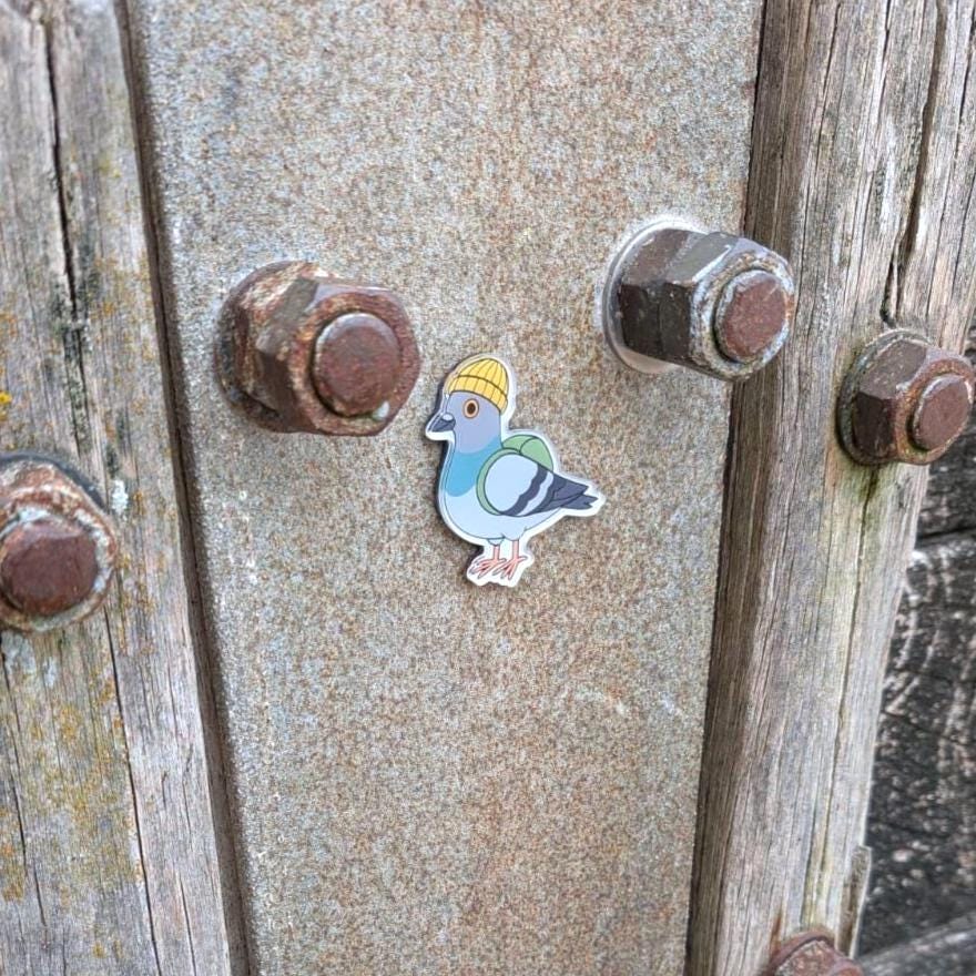 Fridge magnet of a pigeon wearing a hard hat on a metal surface with rusted bolts.