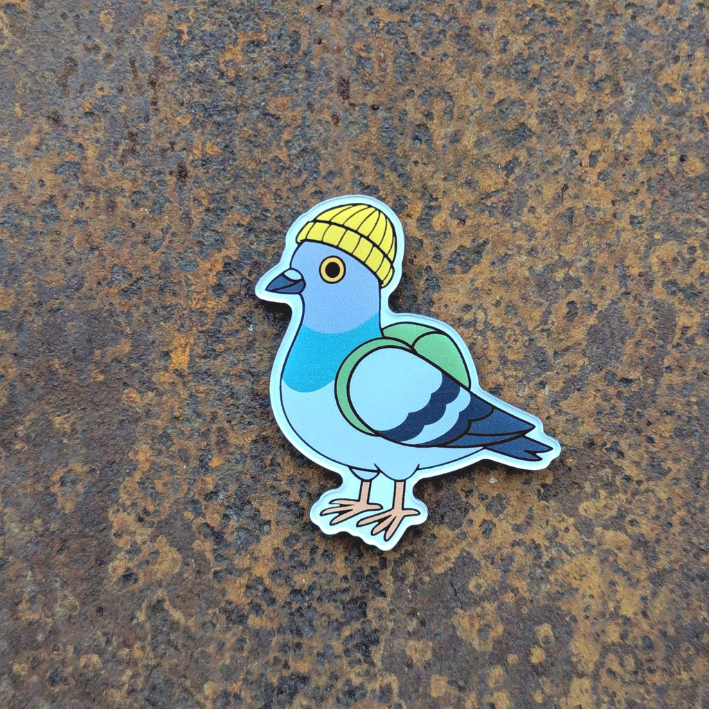 Fridge magnet of an urban pigeon wearing a yellow beanie on a textured brown surface