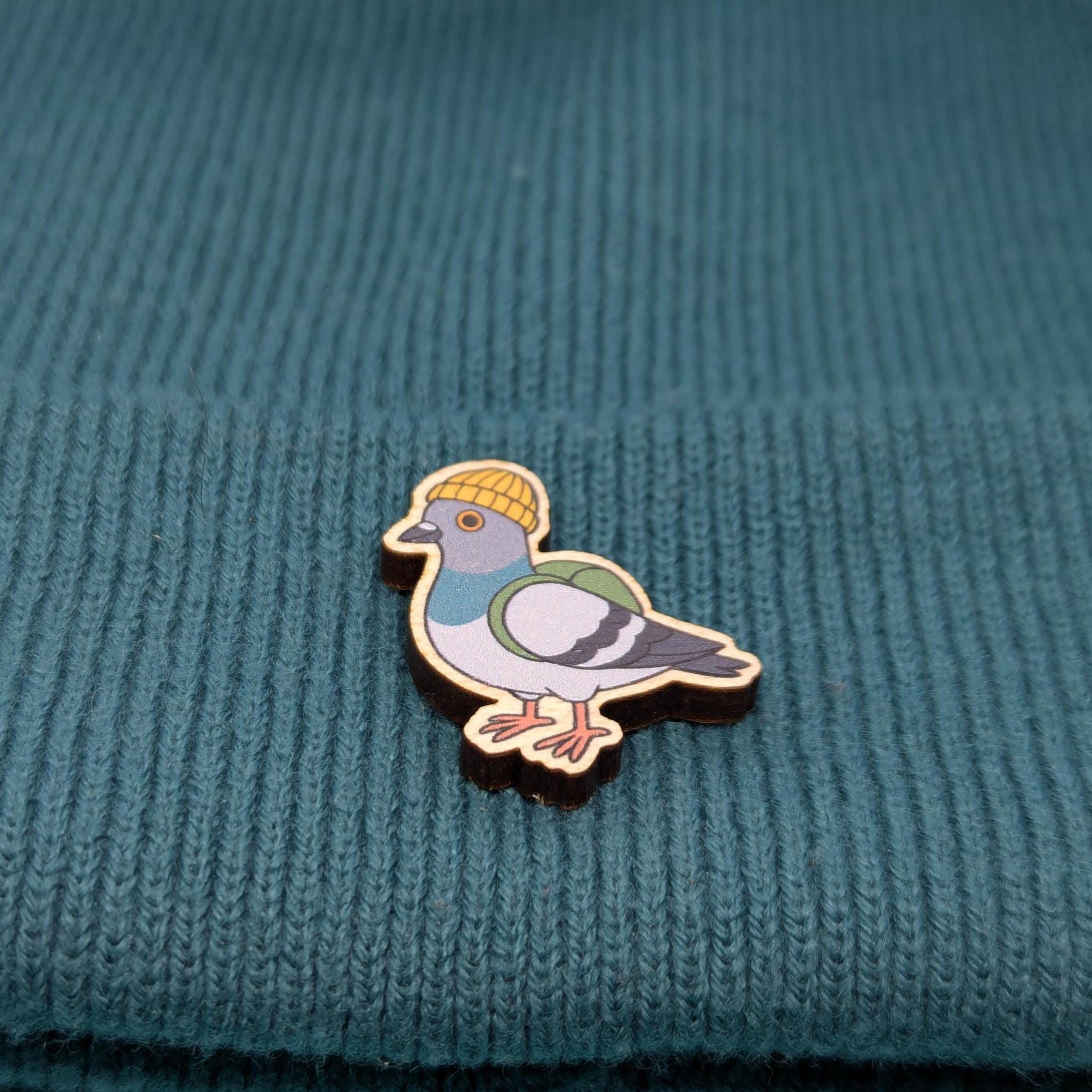 Wooden pin of a pigeon wearing a yellow beanie on a textured teal fabric background