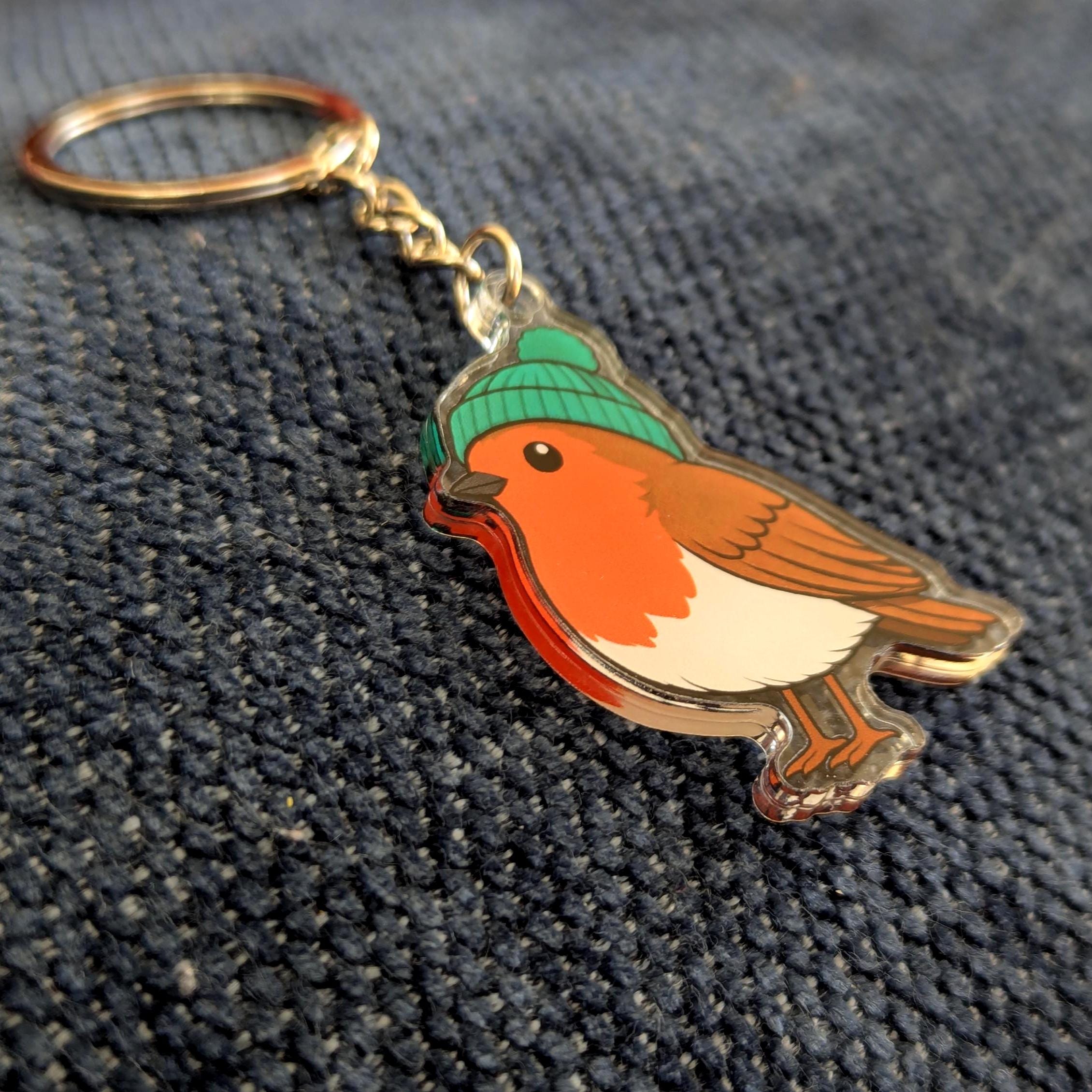Keychain with a robin bird wearing a green hat on a textured dark surface