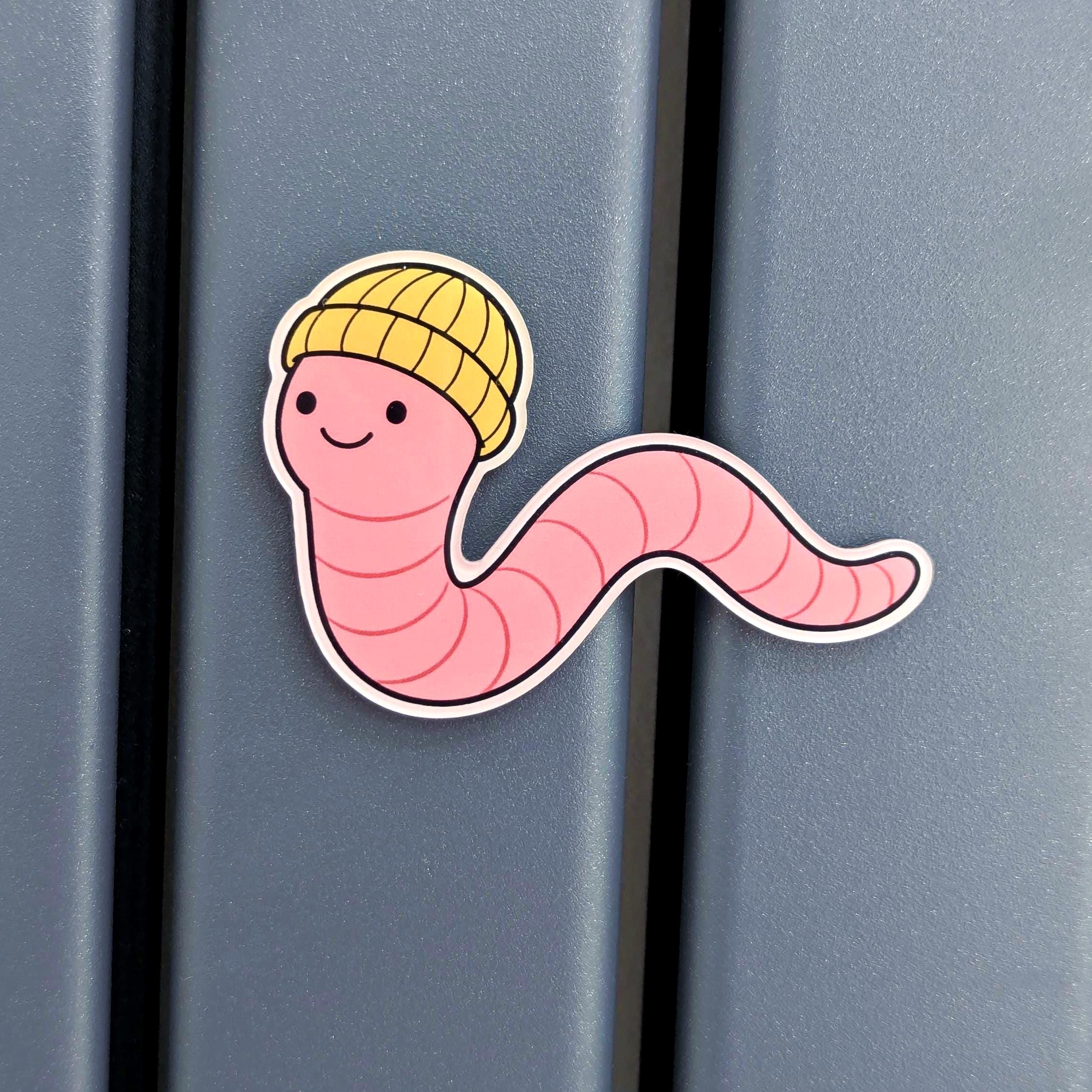 Fridge magnet of a pink worm with a yellow beanie on a blue surface