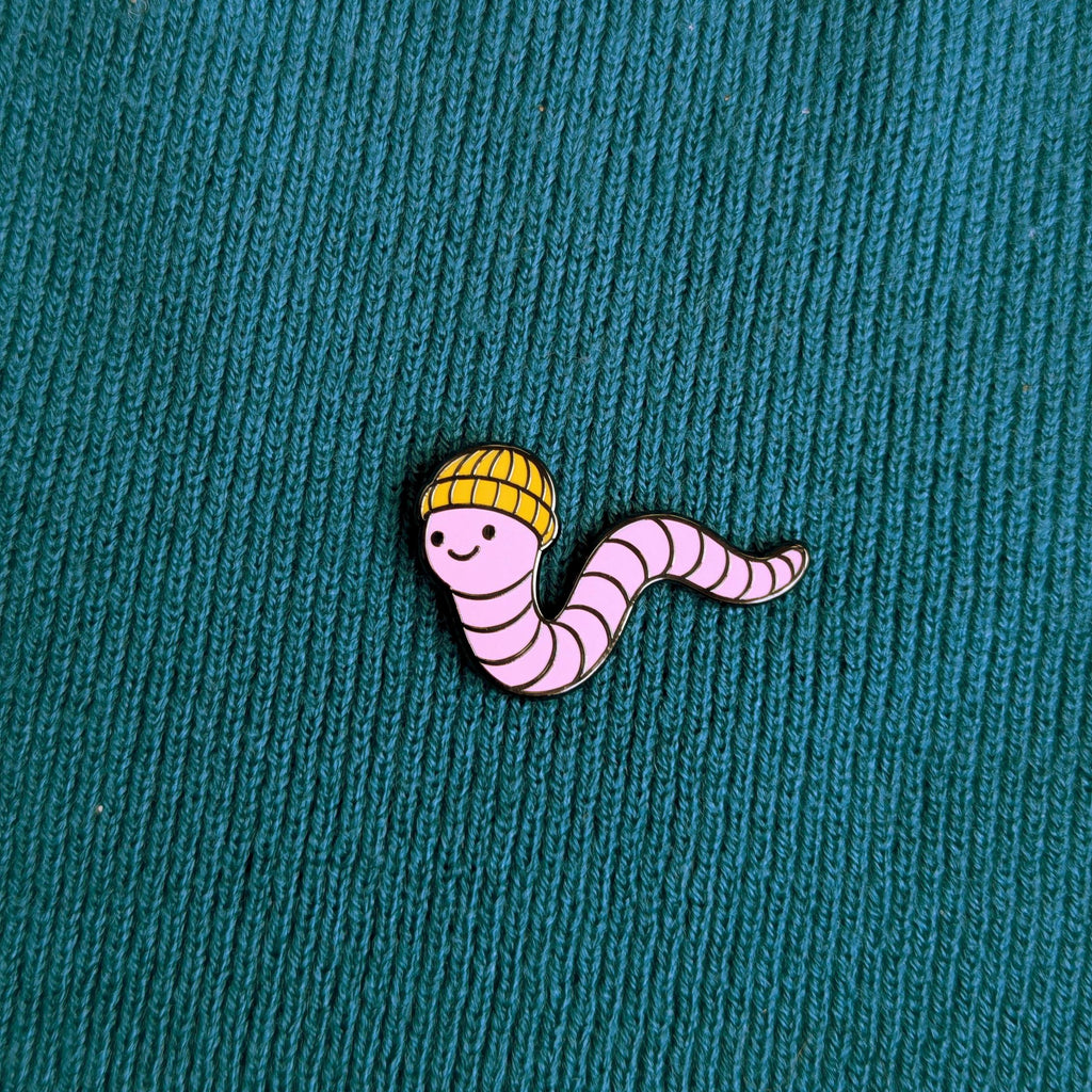 Pin of a cartoon worm wearing a yellow hat on a textured teal background