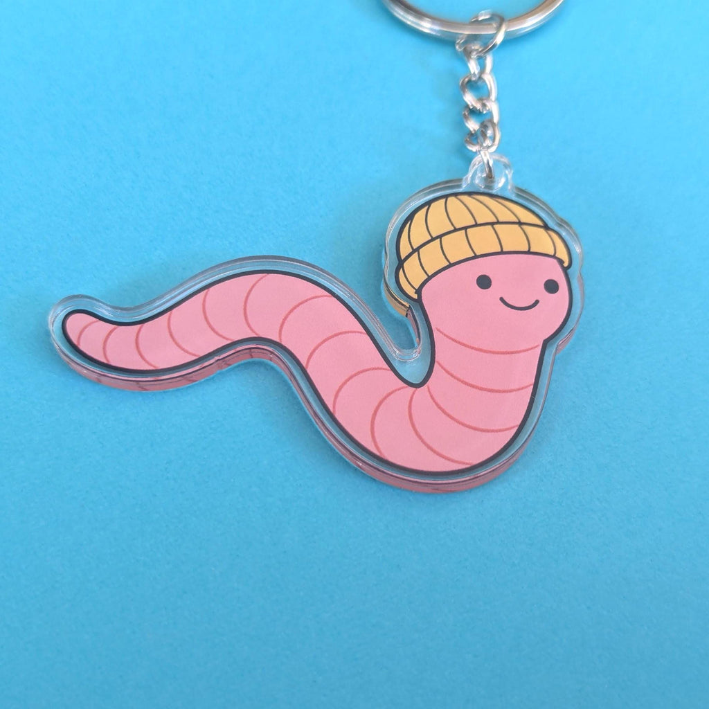 Keychain with a pink worm design wearing a yellow beanie on a blue background