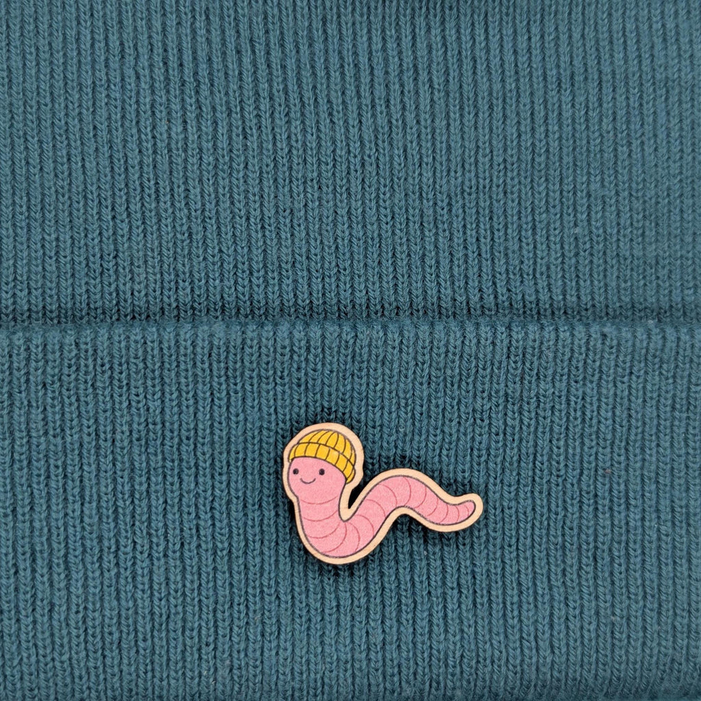 Pink worm with a yellow hat wooden pin on a teal knitted background
